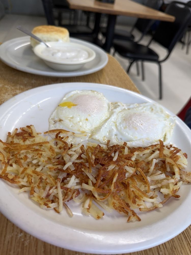 Two fried eggs over crispy hash browns, with a biscuit and gravy behind